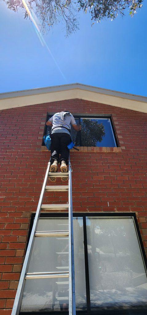 Window cleaner working by hand on an upper-storey window of a brick home