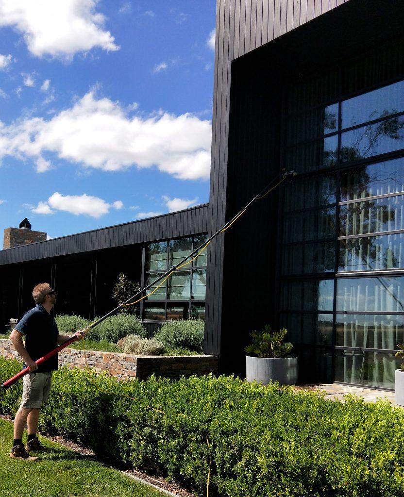 Excel Window Cleaning technician using a water-fed pole to clean the windows of a modern home